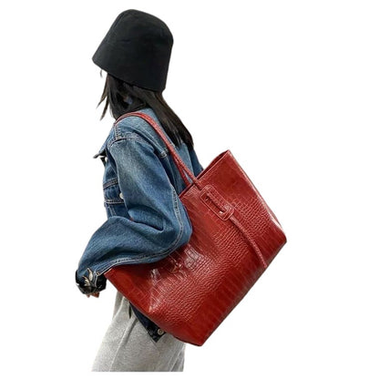 A woman is carrying a deep red croc-embossed vegan leather tote bag over her shoulder.