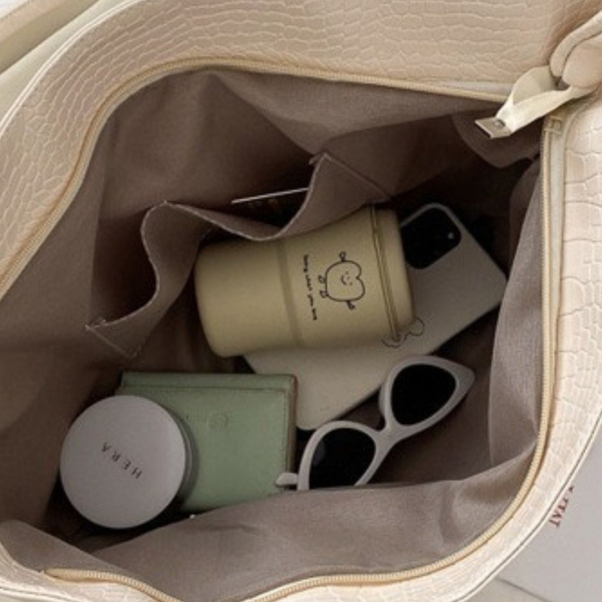 Opened off-white croc tote with sunglasses, phone, and wallet inside, showing internal slip pocket.