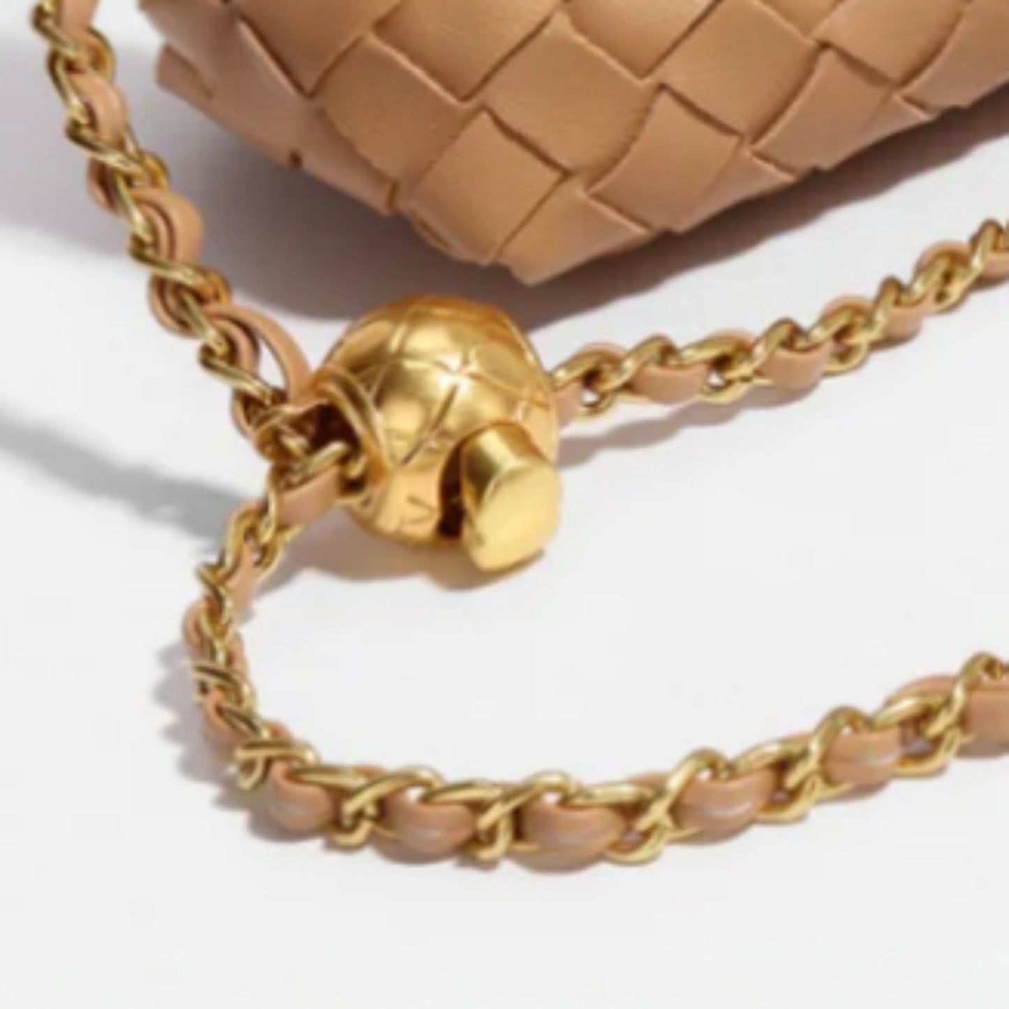 Display of a hand-woven vegan leather bag with a gold chain and an adjustable spherical clasp. 