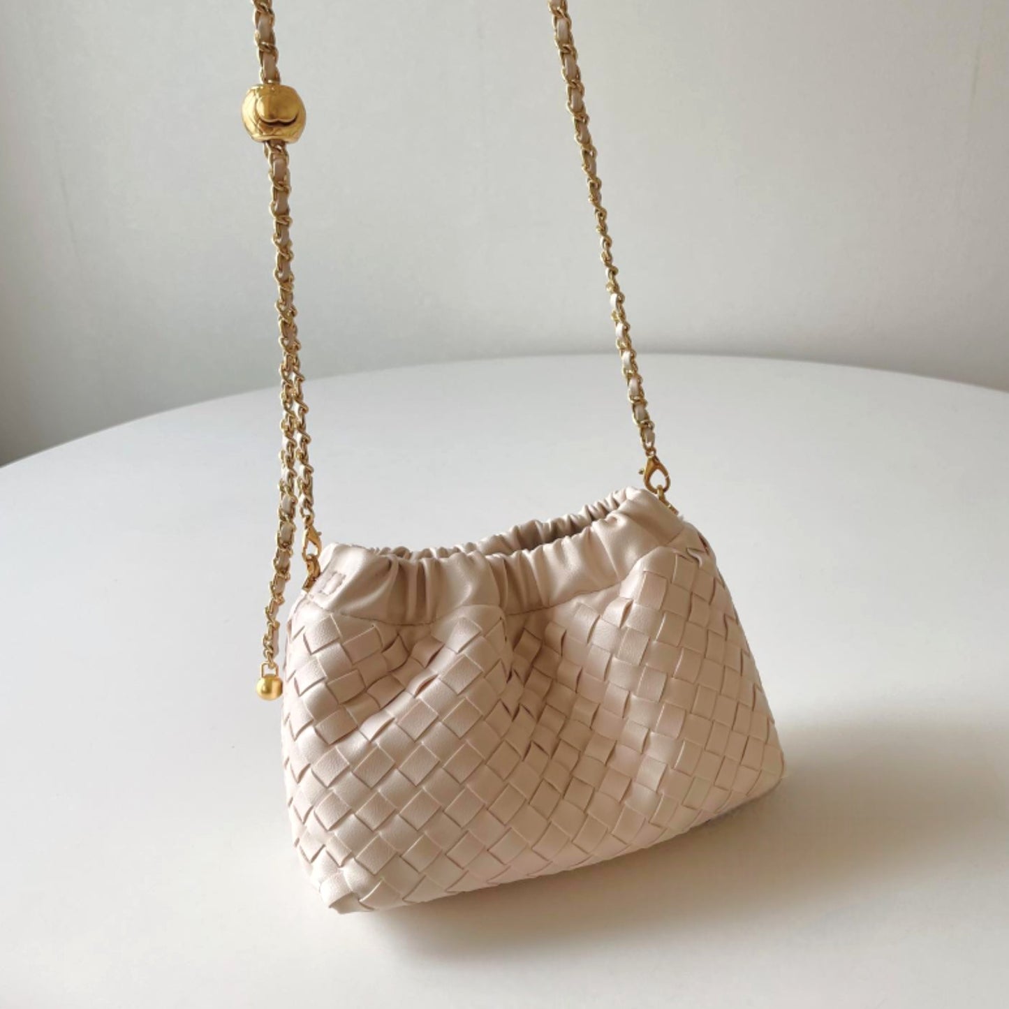 An everyday casual cream-coloured hand-woven shoulder bag with a gold chain strap on display.