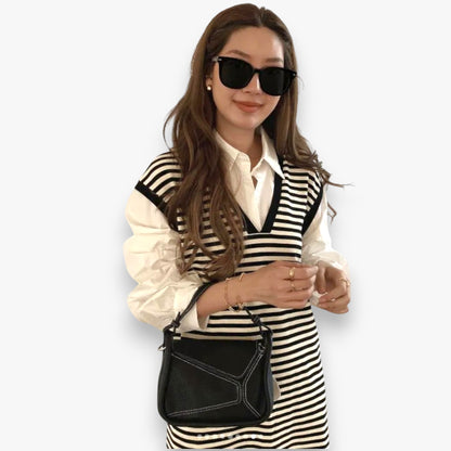 A woman is carrying a small black origami-inspired handbag on her arm.