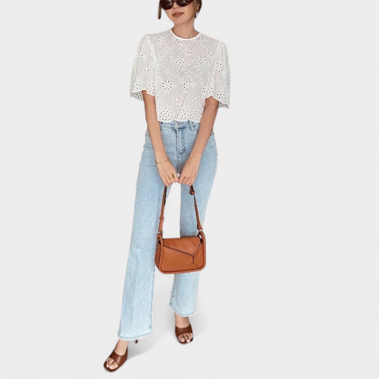 A woman carrying a strap of a small brown handbag with a geometric design in front of her.