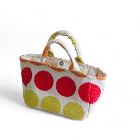 The top view of a tote bag with vibrant red, green, and orange dots on beige fabric and light-coloured lining.