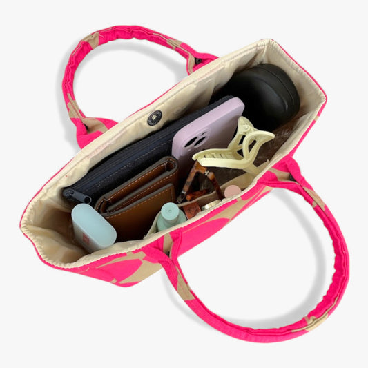 Top view of a pink-and-beige women's handbag with compartments containing everyday items.