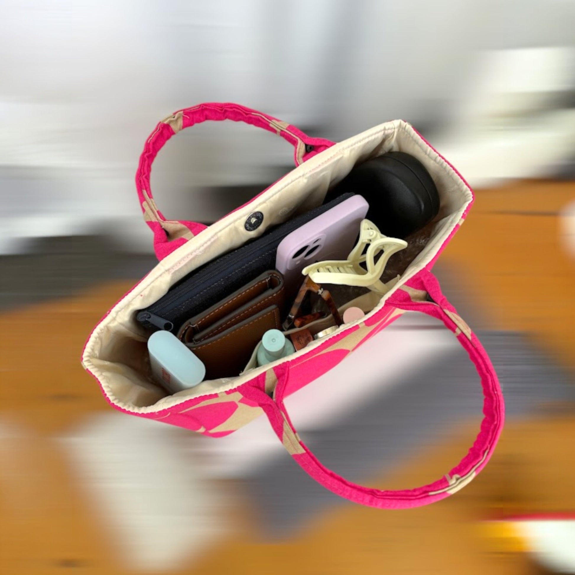 A pink and beige polka dot handbag on a blur background with everyday essential items inside.