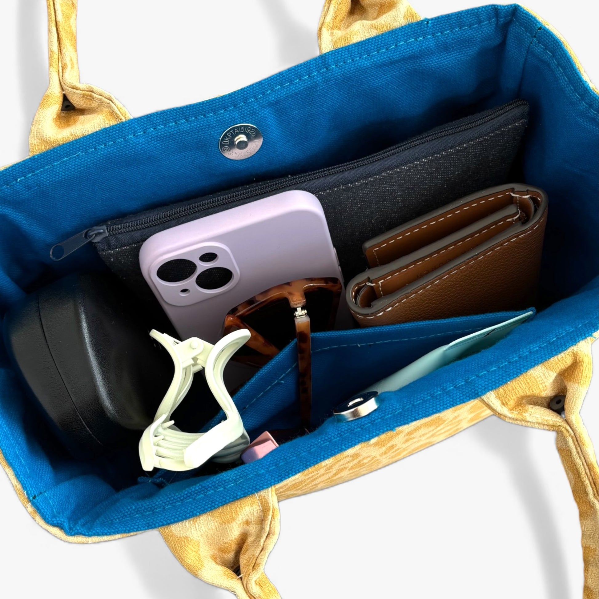 An open, spacious mini tote bag with top handles and blue lining, revealing everyday items inside.