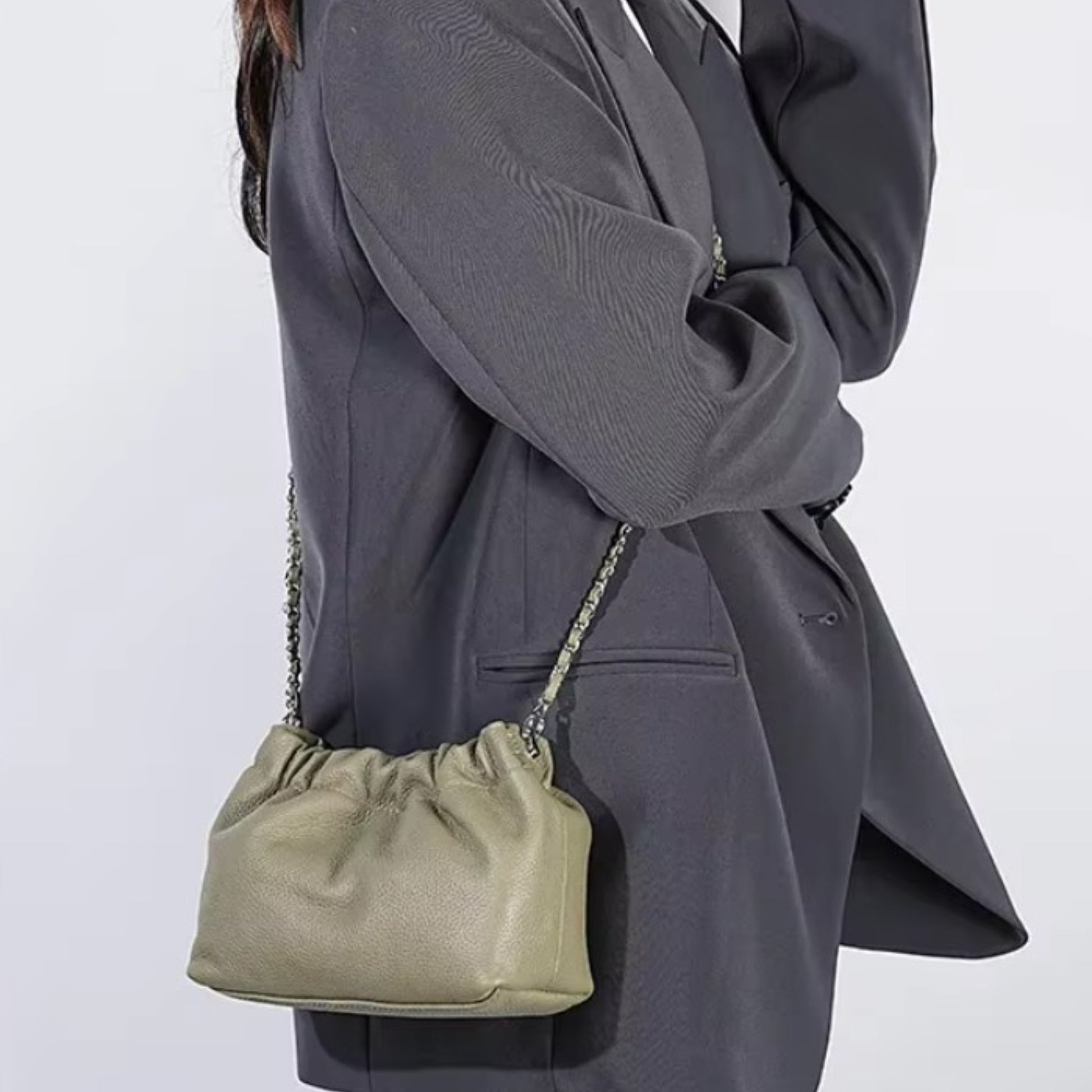 Close-up of a person carrying an olive ruched-opening stylish leather bag with a silver chain strap.