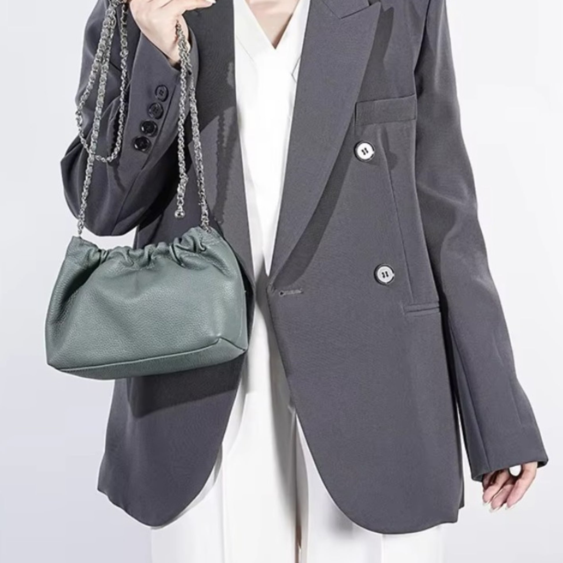 Close-up of a person holding a blue grey ruched-opening stylish leather bag with a silver chain strap.