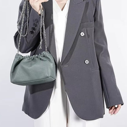 Close-up of a person holding a blue grey ruched-opening stylish leather bag with a silver chain strap.