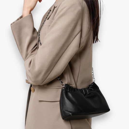 Close-up of a person carrying a black ruched-opening stylish leather bag with a chain strap across her body.