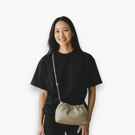 A woman carries a beige shoulder bag with a ruched opening and a chain strap across her body.