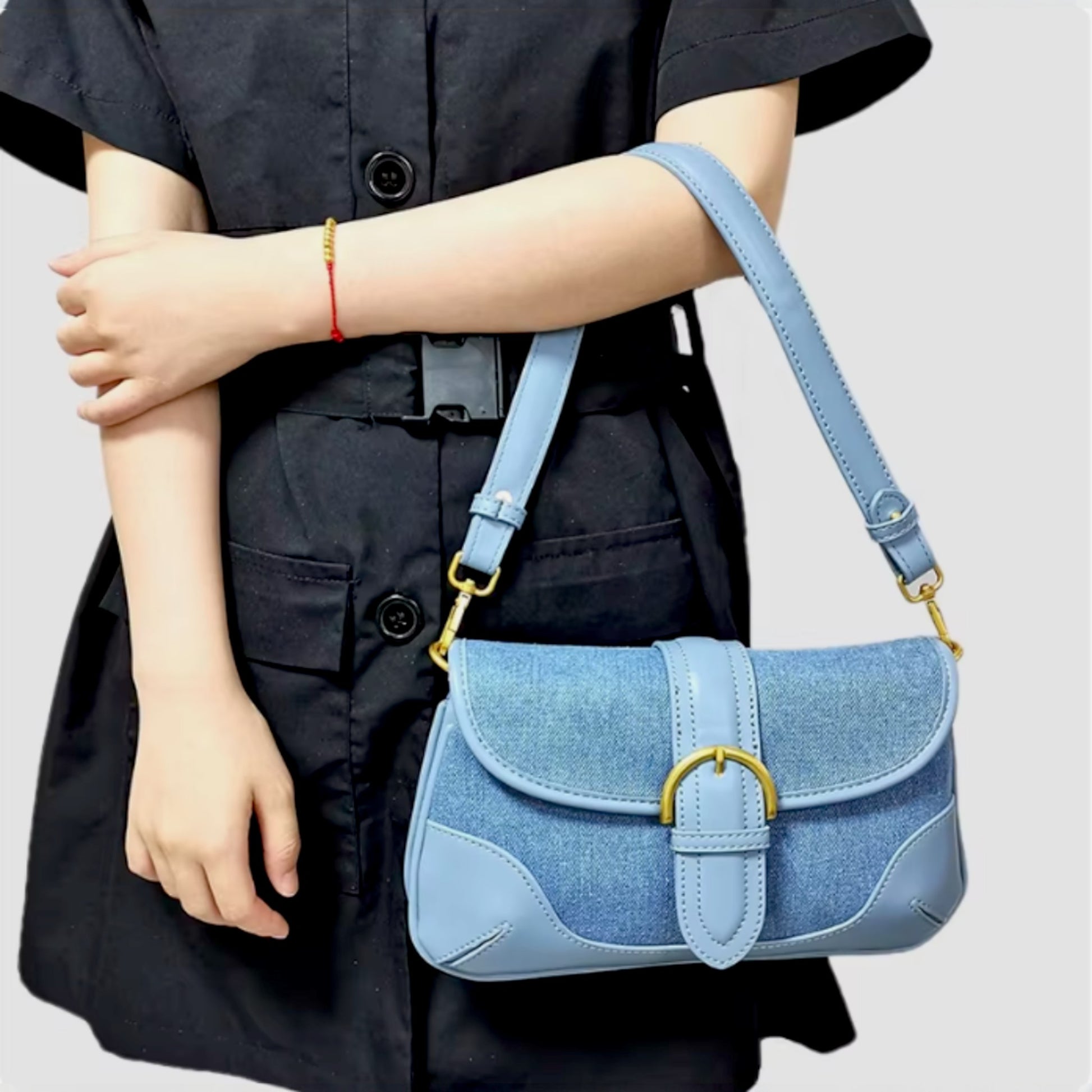 A woman carries a blue denim shoulder bag in the crook of her arm. The bag features leather trims and brass details.