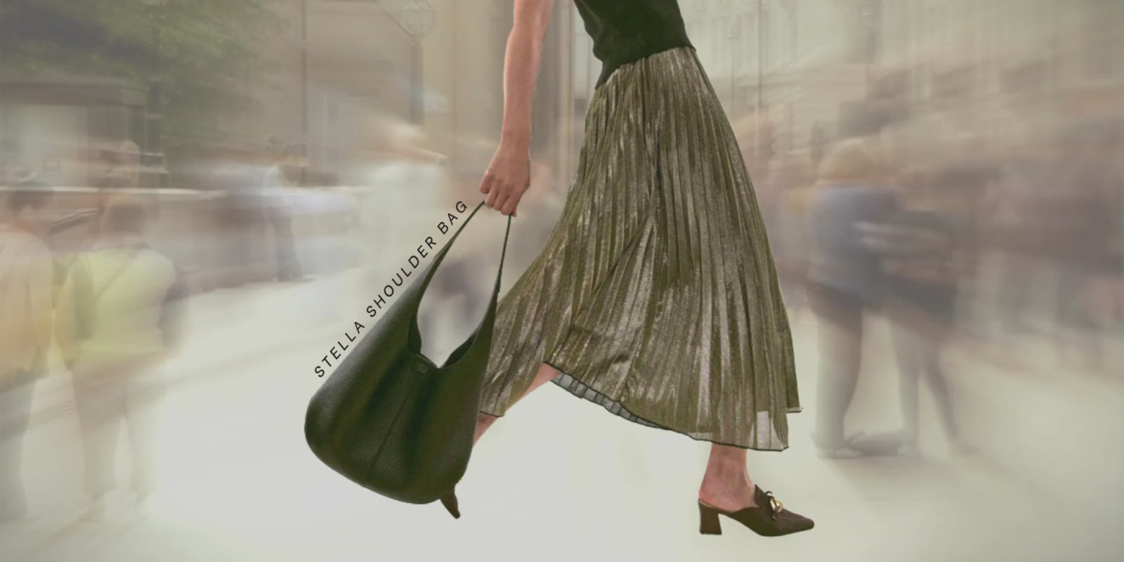 Load video: Woman carrying STELLA black boho-style shoulder bag, while people walking past in the background.