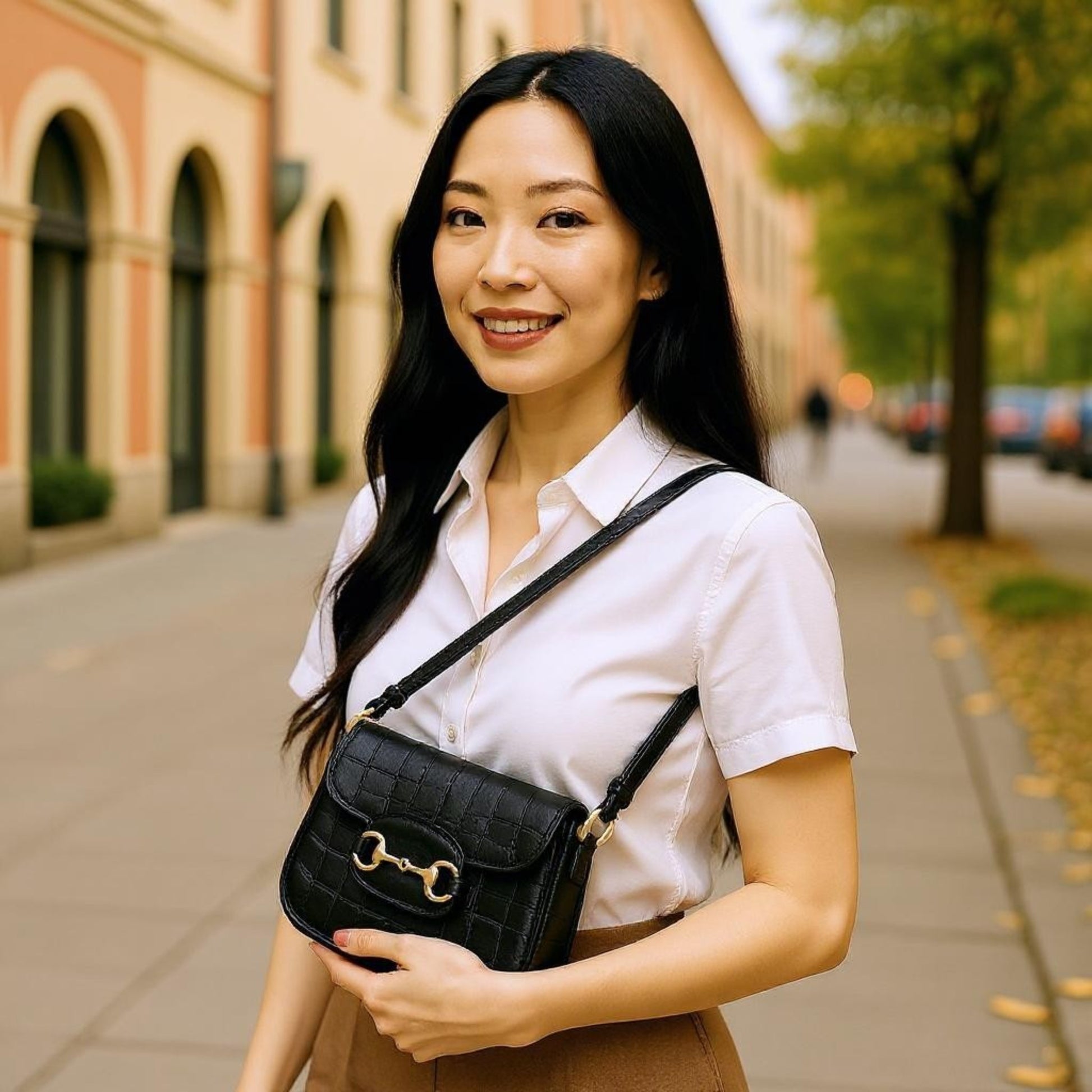 A woman carries a black crocodile-embossed bag with gold horsebit over the shoulder.