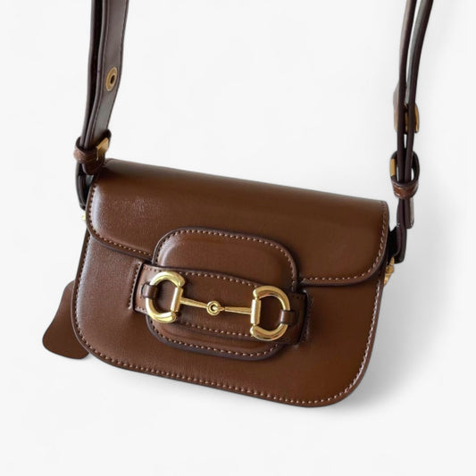 An elegant equestrian-style brown bag with gold horse-bit buckle detail.