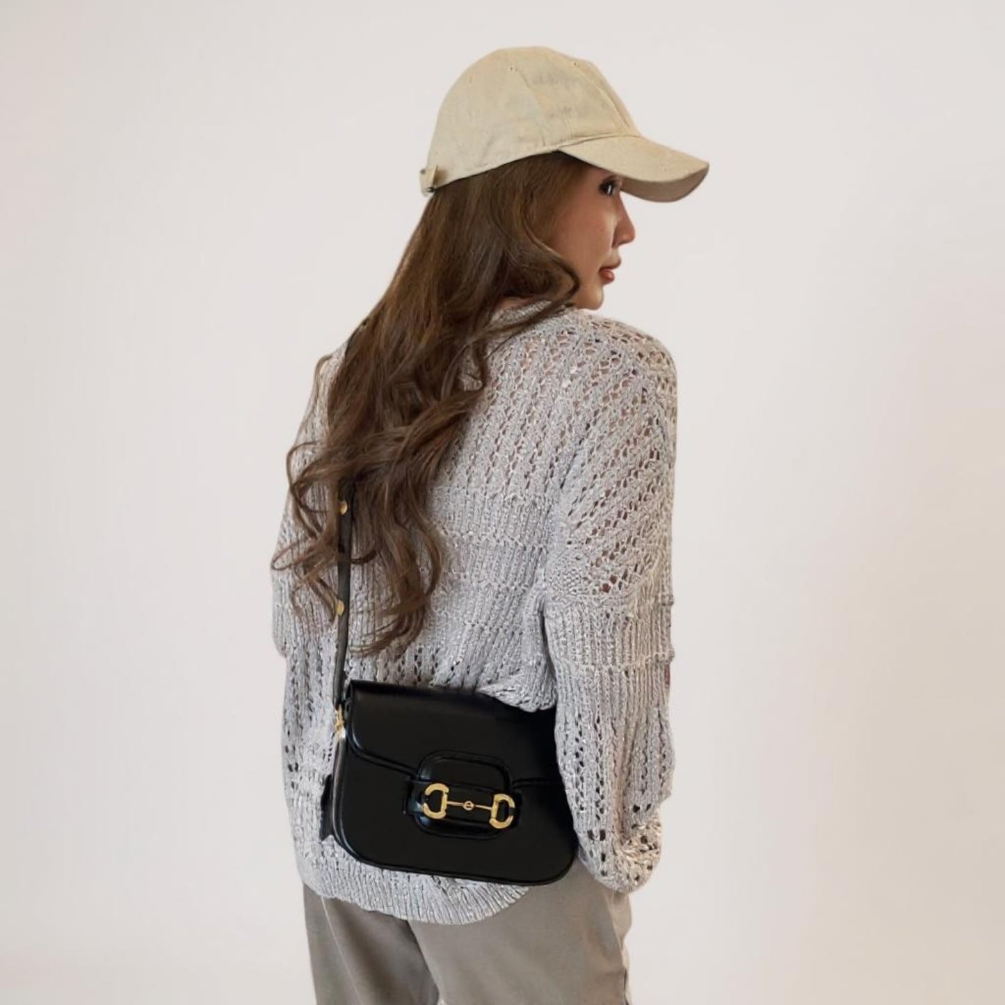 A woman wears a sophisticated black vegan leather bag with gold hardware across her body.
