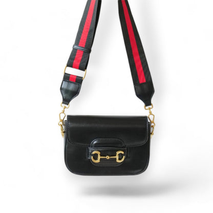 A black leather handbag with a wide red and black nylon strap hanging on the wall.