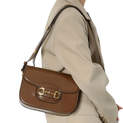 A person carrying an classic horse bit flap top shoulder bag with gold hardware on her shoulder.