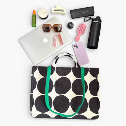 A black and white polka dot tote bag with handles and a green strap. Large enough for a laptop and daily carry.