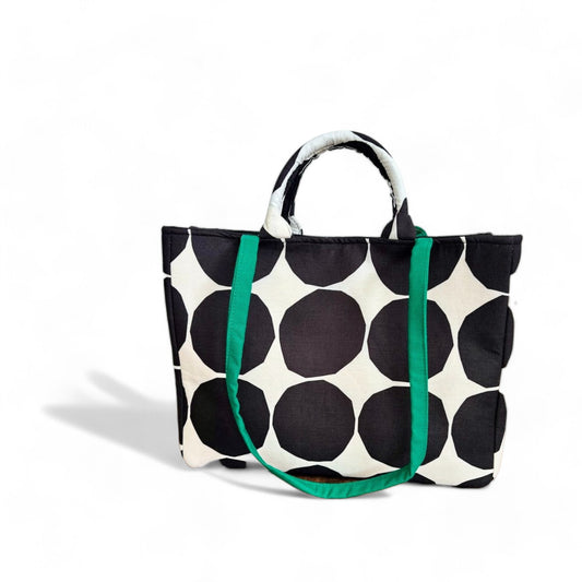 A white shopper tote bag with a big black polka dot pattern and green shoulder straps.