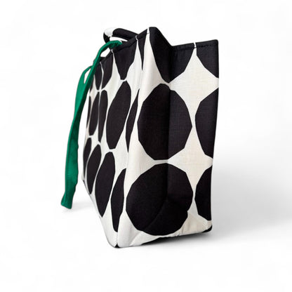 Side view of a back and white polka dots tote showing a green shoulder strap.