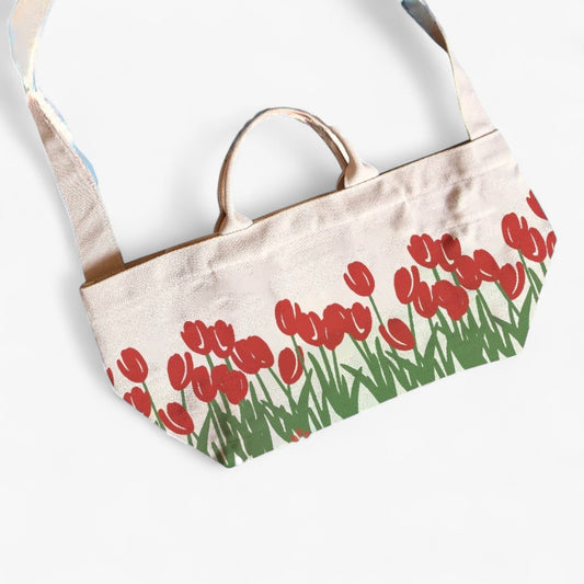 A flat lay of a canvas shopper tote bag with red tulip prints, a shoulder strap, and top handles.