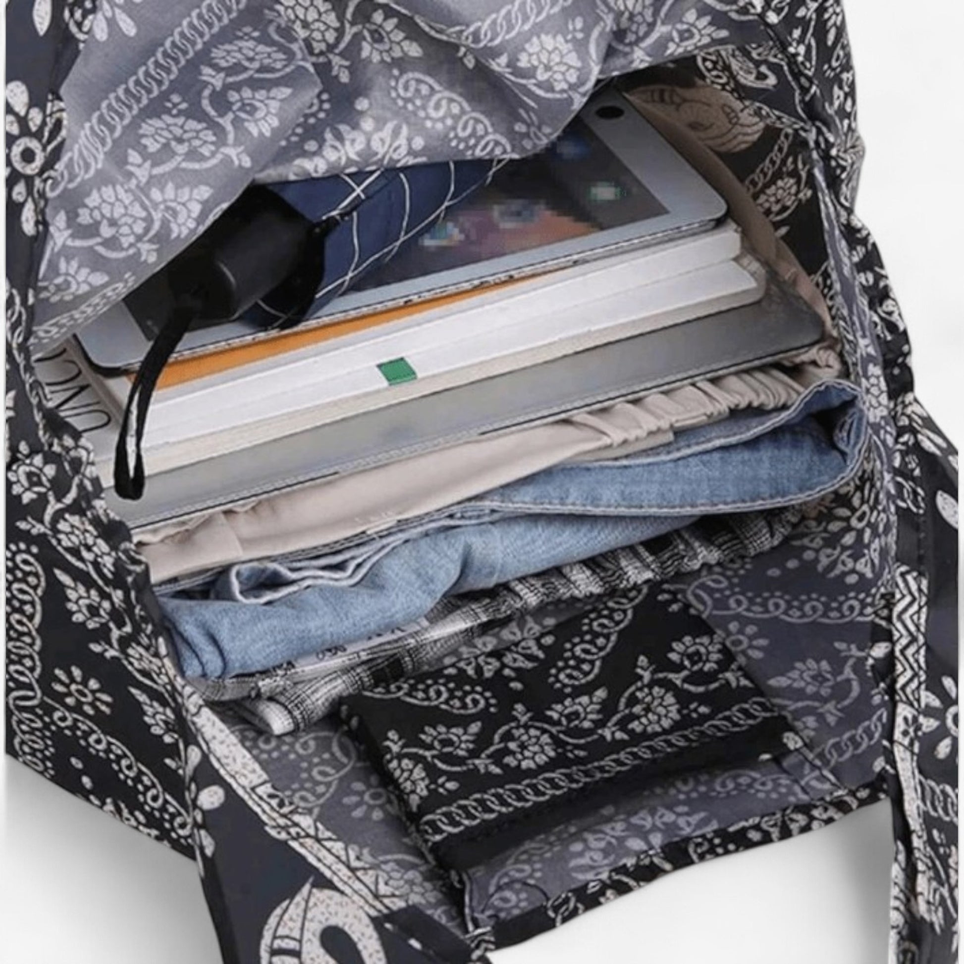An open, dark brown and white elephant pattern tote bag containing a laptop, books, an umbrella, and clothes.