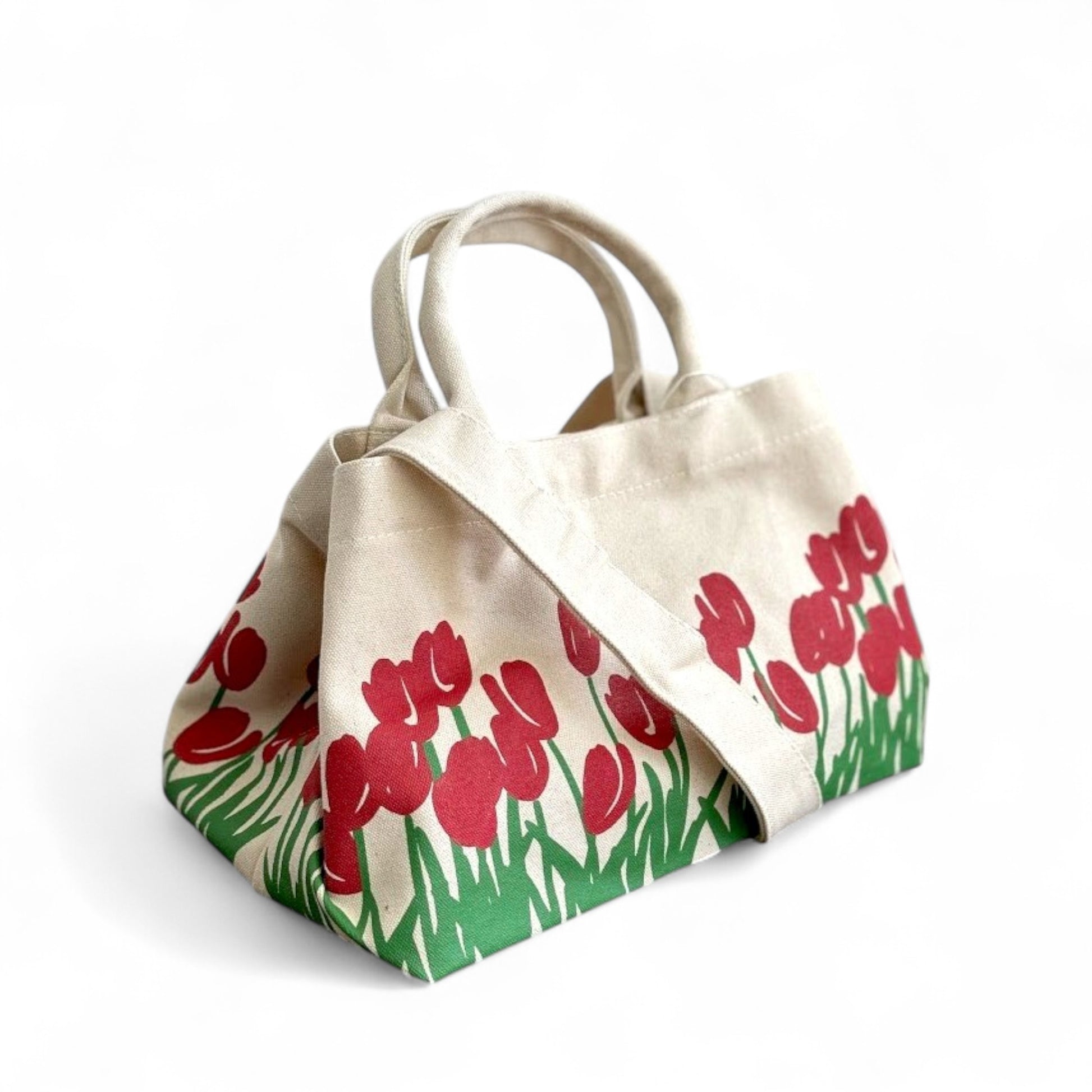 Side angle view of a shopper tote bag with red tulip prints, top handles, and a shoulder strap.