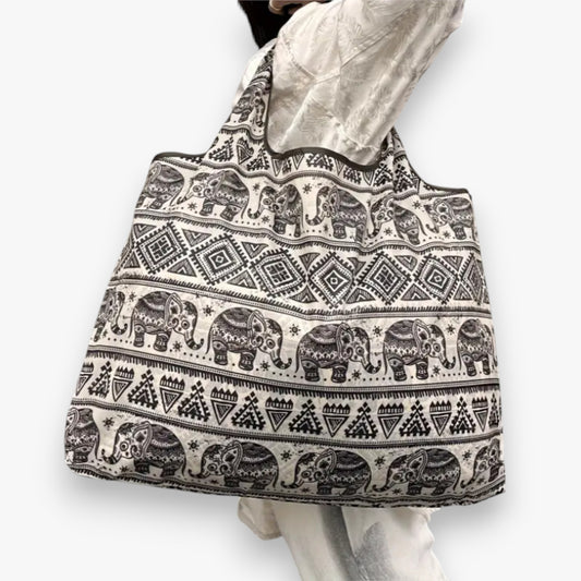 A person carrying a light brown shopping tote bag with brown elephant patterns on the shoulder.